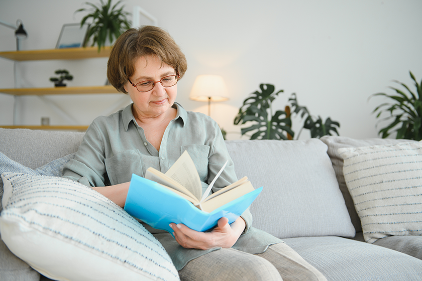 Old lady sitting on couch and enjoying interesting novel