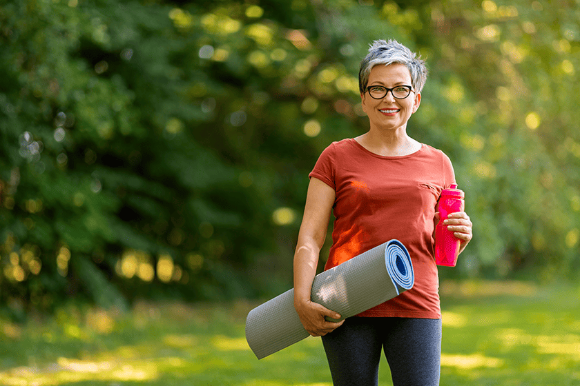 smiling senior woman holding water bottle yoga mat