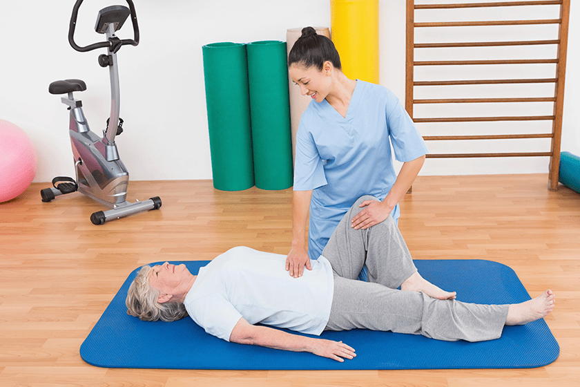 therapist working with senior woman on exercise mat